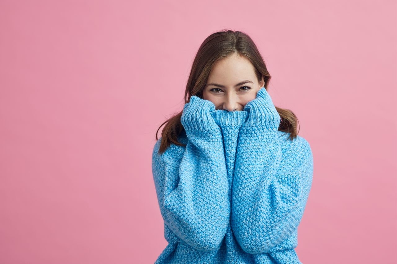 Woman laughs and pulls her sweater over her mouth to hide – symbolizing overcoming fear – A1 German course speaking practice in Frankfurt