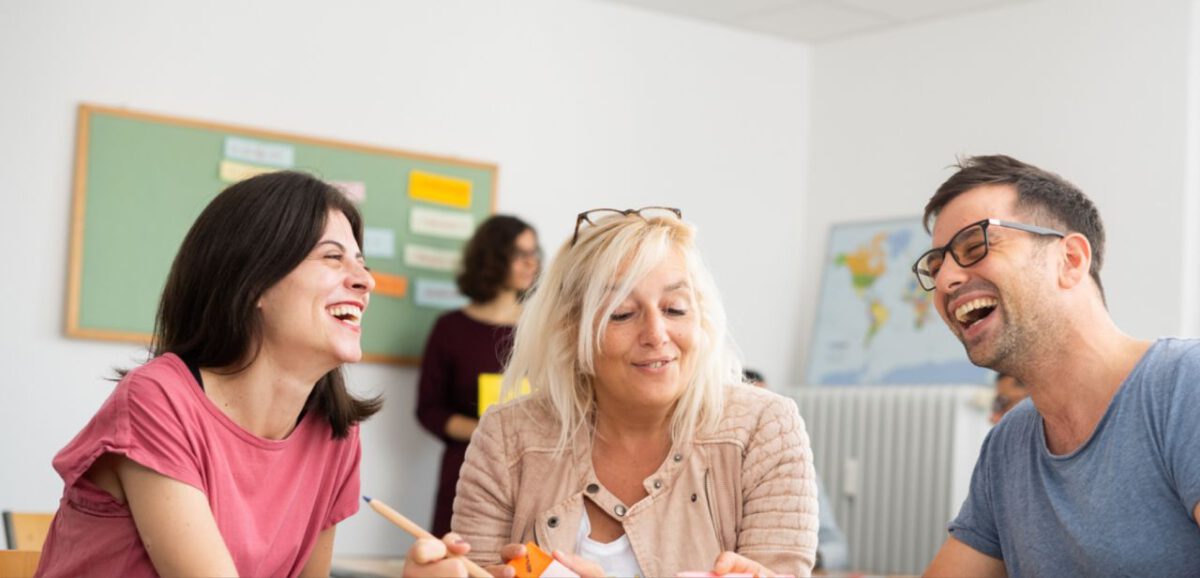 Kursteilnehmer sprechen und lachen im B2 Deutschkurs in Frankfurt am Main, kleine Gruppe mit Lehrerin im Hintergrund