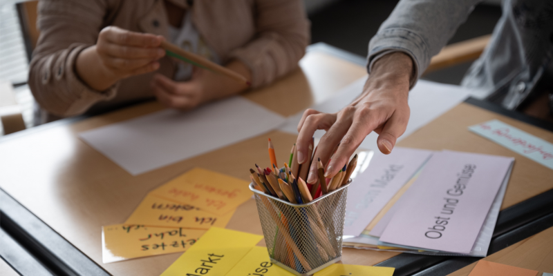 Hände von Kursteilnehmern im Vormittags-Deutschkurs in Frankfurt, Stifte und Wortkarten auf dem Tisch