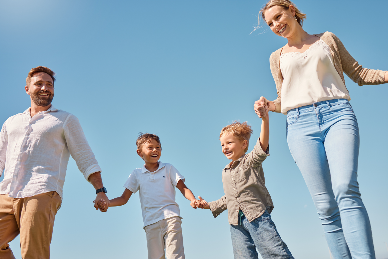Glückliche Familie mit zwei Kindern läuft lachend über eine Wiese beim Deutschlernen für Kinder
