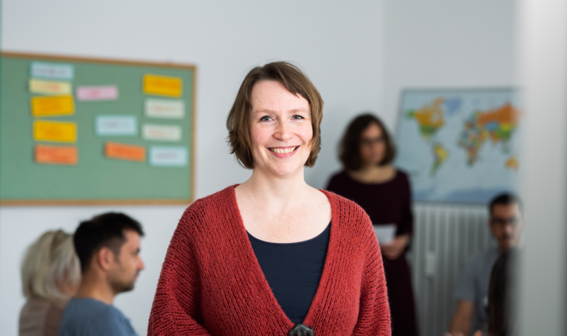 Franziska Becker, founder of SprachPassion language school in Frankfurt, during an evening German class. In the background, a teacher is teaching while learners listen attentively.