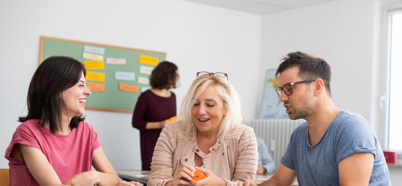 Three participants in a morning German language course in Frankfurt in a small group with teacher in the background